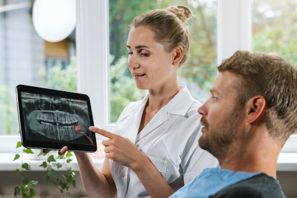 Dentist explaining an impacted wisdom tooth on an X-ray to a patient.