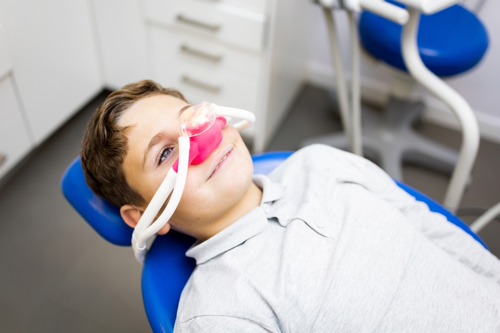 A little boy sits in a dentist's office wearing a nasal mask to breathe nitrous oxide to relax