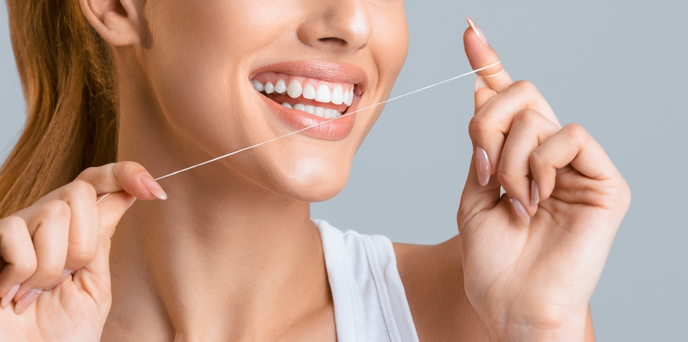 Cropped of a young woman flossing her teeth with a white flos